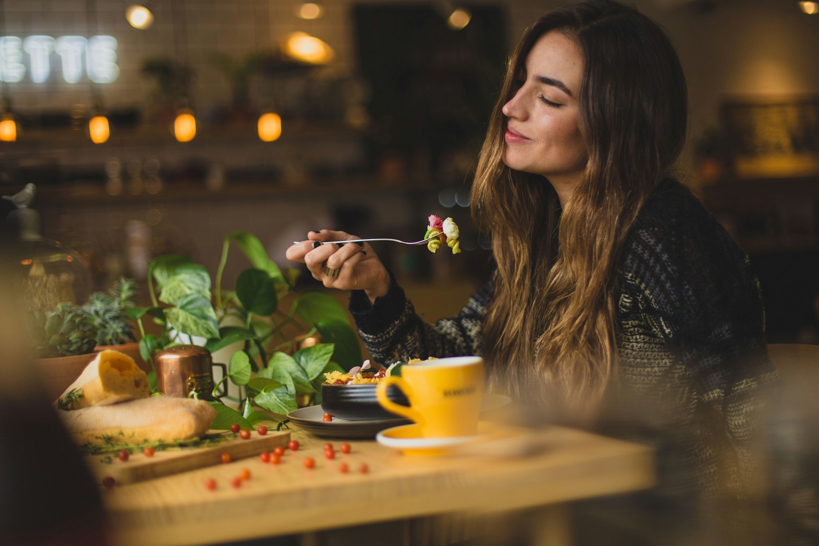 Woman savoring a bite of food in a warmly lit cafe.