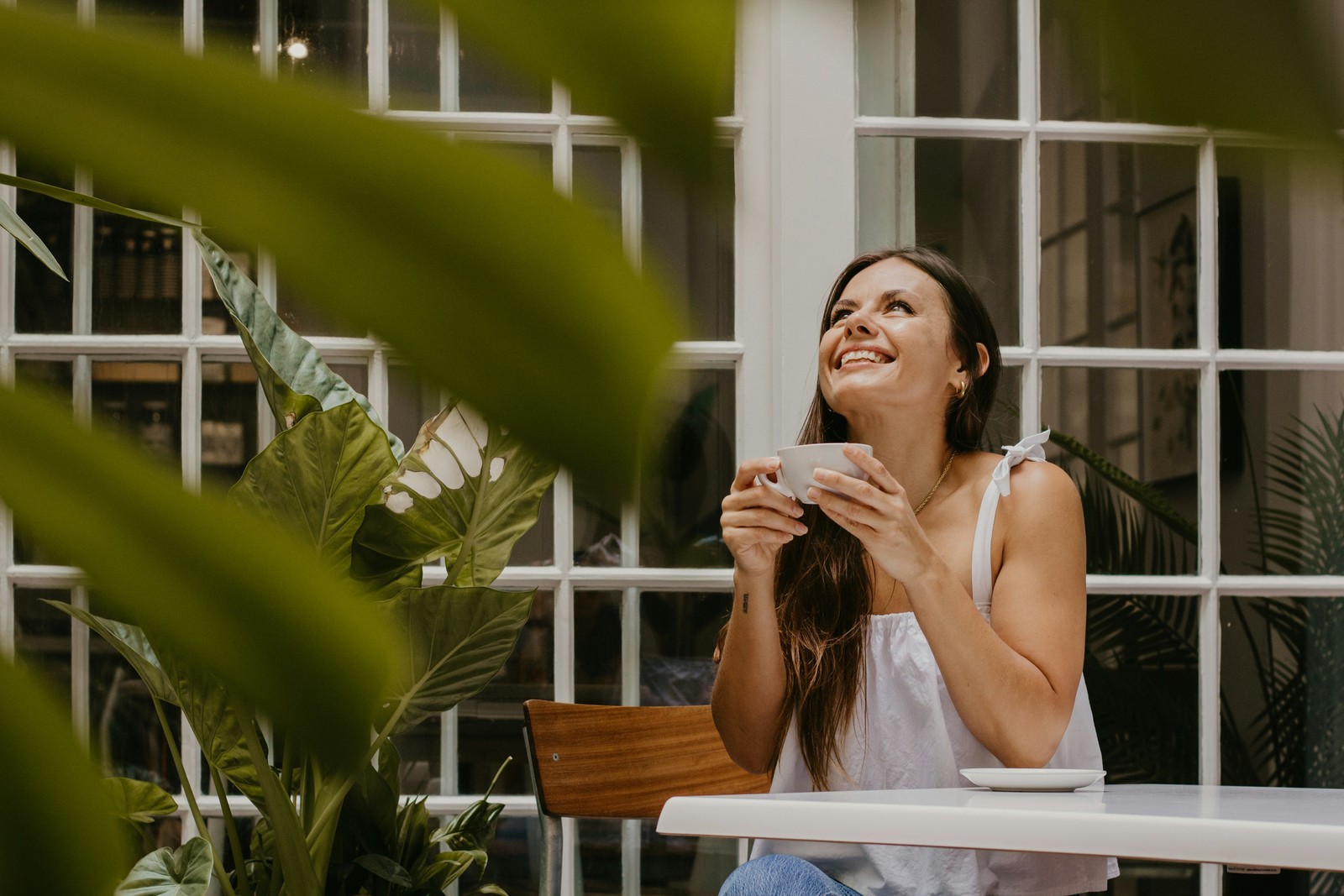 Woman with tea, looking up smiling, plants in foreground.
