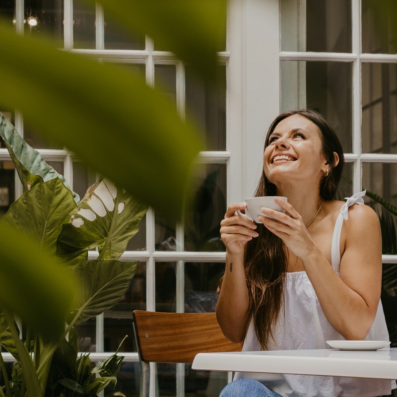 Woman with tea, looking up, plants in foreground.
